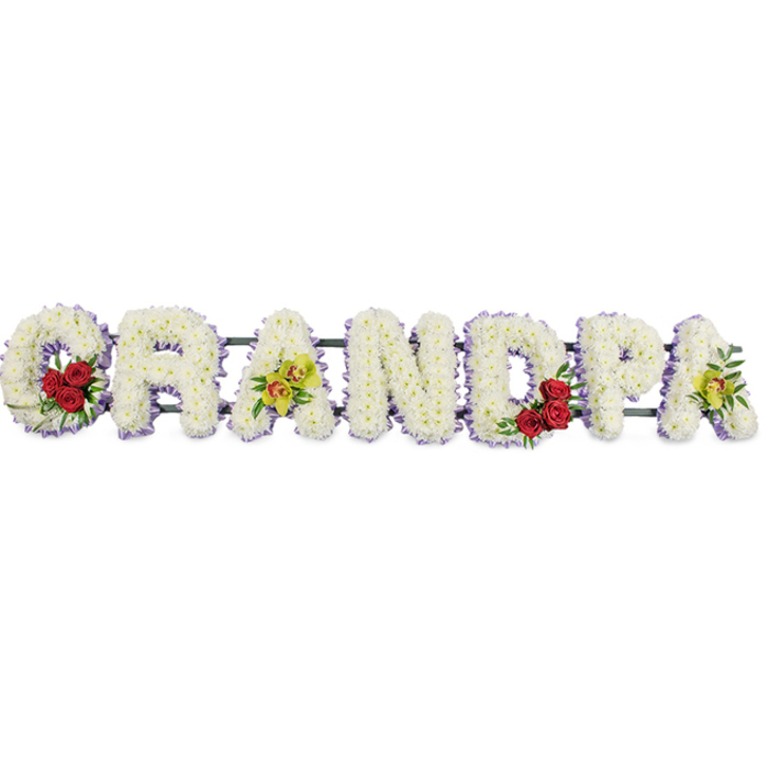 The image shows a refined funeral tribute in the form of the word GRANDPA, crafted as individual capital letters arranged in a straight line. Each letter is generously covered with compact white chrysanthemums, creating a continuous, cushion-like surface that feels soft to the eye, almost like pressed snow or a folded blanket of petals. This floral lettering is set against a stark white background, which intensifies the contrast and allows every contour, colour accent, and ribbon edge to be read clearly, as though viewed in the calm light of a chapel in Charlton before mourners arrive. Around the edge of each letter runs a narrow band of lavender-purple ribbon, giving a clear outline that helps each character stand apart while still contributing to the overall harmony of the piece. Within the comforting white base, the florist has introduced small but expressive arrangements: the curving sections of the G and D cradle clusters of rich red roses, their velvety petals forming compact hearts of colour that symbolise deep affection and gratitude. The first and last A are embellished with yellow-green orchids, some petals showing subtle red or brown touches in the centre, lending a graceful, almost ceremonial elegance. The letters are supported and aligned on a discrete dark frame, with thin bars linking them to ensure the word remains stable when displayed at the front of a funeral service or laid beside the grave. This detailed and personalised design feels like a thoughtful choice for families around Charlton and nearby Greenwich, a tribute that quietly celebrates a grandfather's role at home, in the garden, or on gentle walks through local parks. The interplay of pure white, passionate red, and refined orchid tones creates a lasting impression of peace, honour, and enduring love.